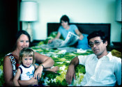 Wilcommen, No. 0035 A Young White Couple Smile for a Photo While Holding a Young Girl In a Hotel Room